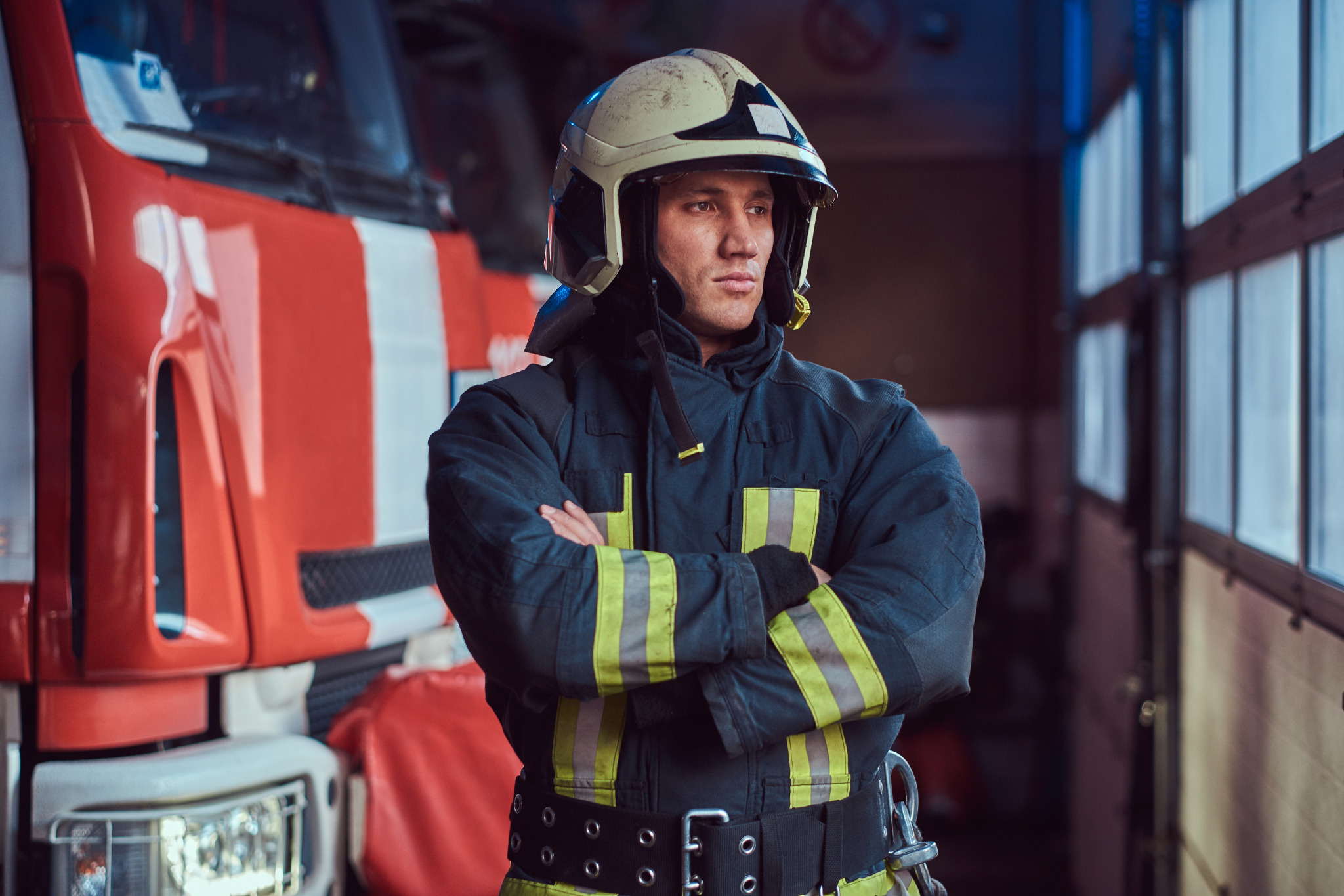 brave-fireman-wearing-protective-uniform-standing-fire-engine-garage-fire-department-crossed-arms-looking-sideways