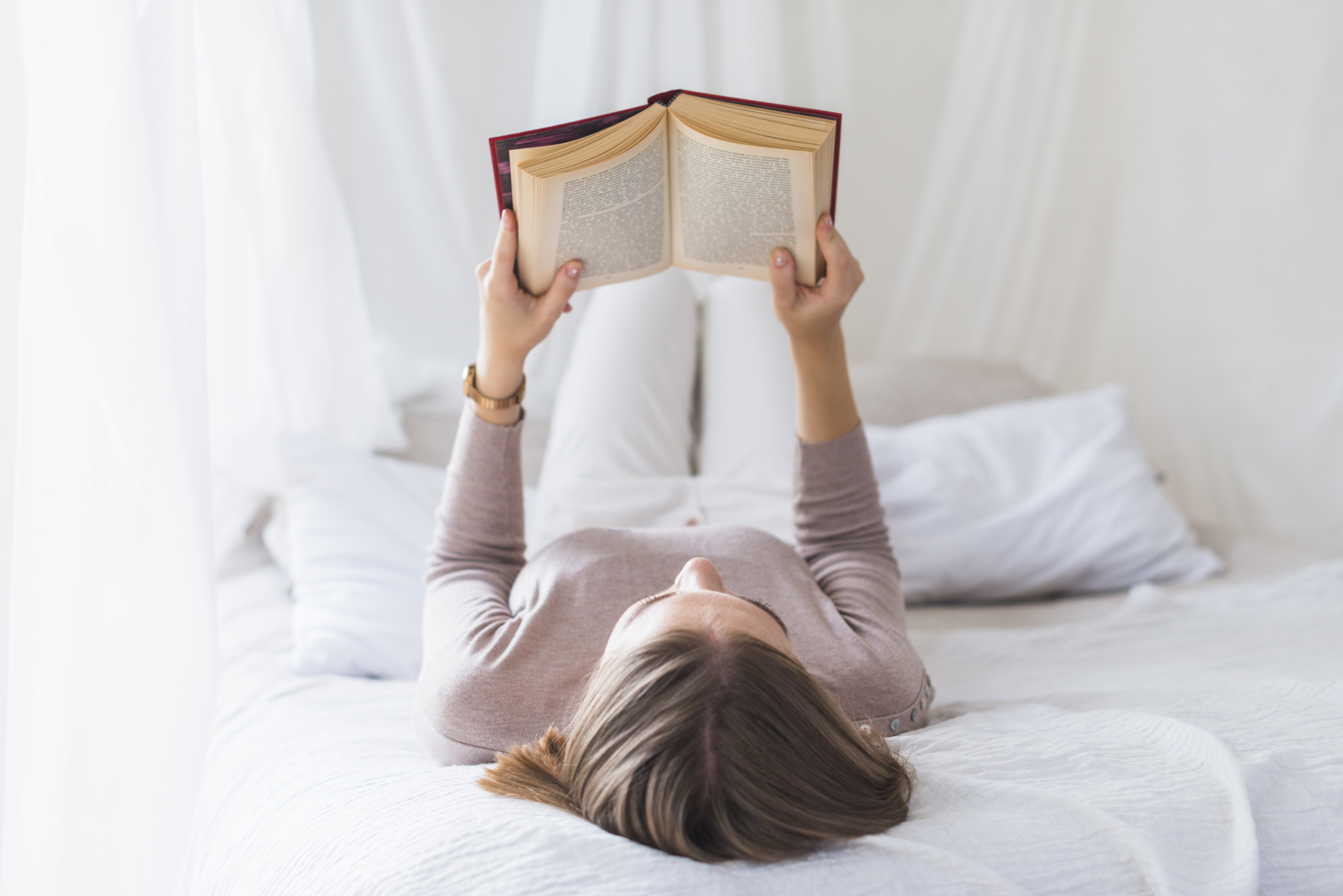 woman-lying-white-bed-reading-book-home